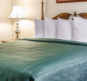 A bed in a hotel room with a green comforter.